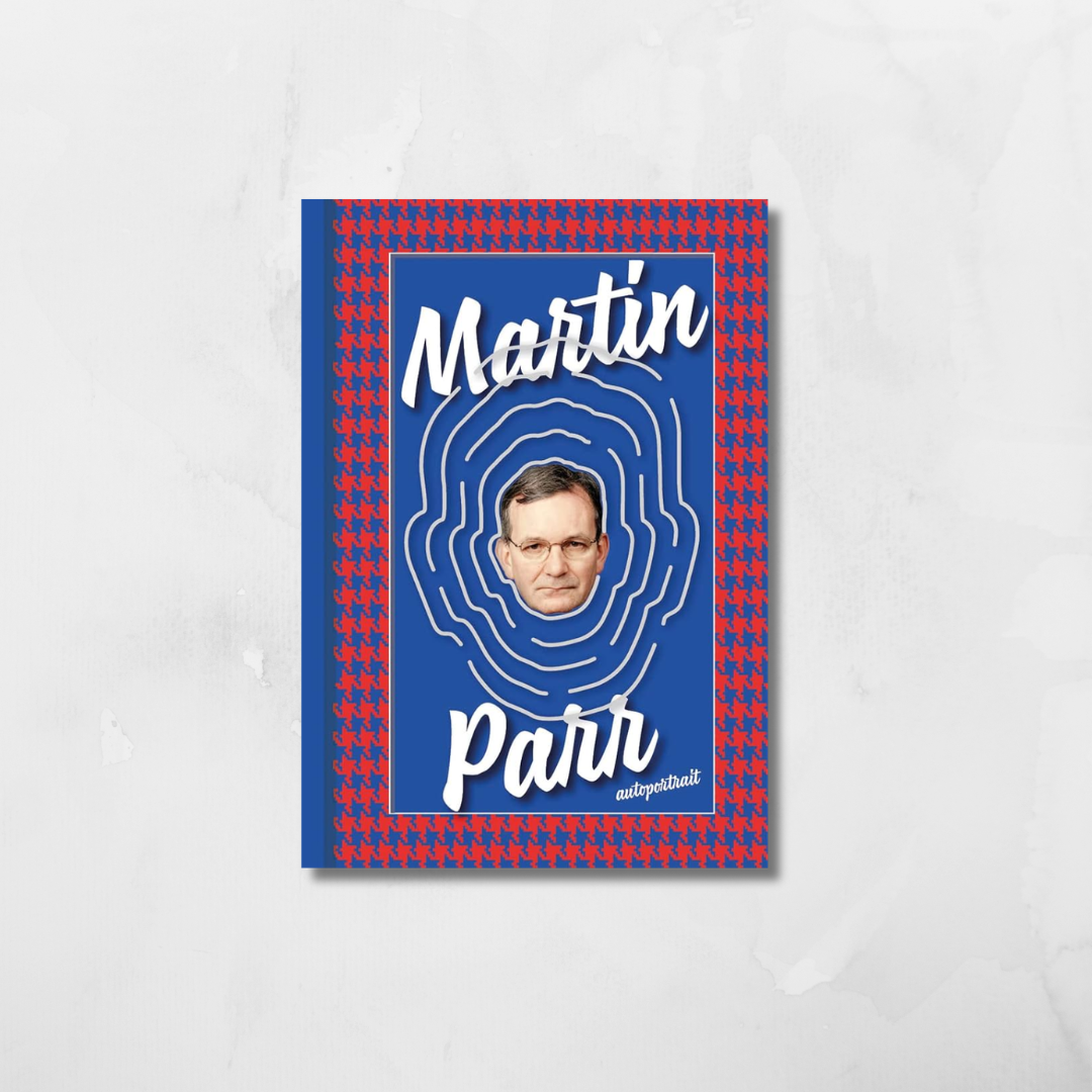 A book cover for 'Martin Parr' featuring a blue background with concentric white fingerprint-like lines, a portrait of Martin Parr in the center, and a red-and-blue checkered border, shown against a light gray marble-textured background.