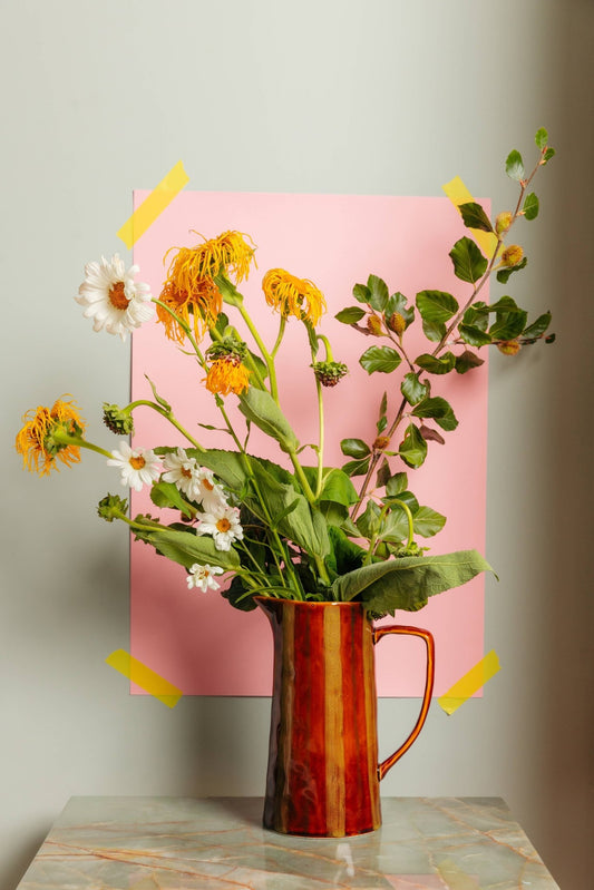 Vase with flowers on a table against a pink background
