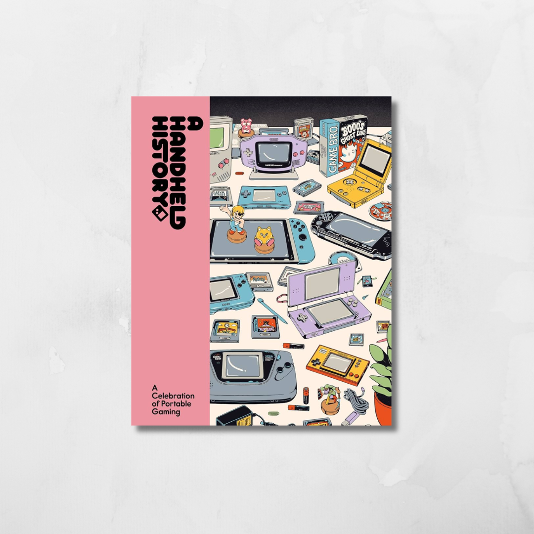 A book or magazine cover titled 'Handheld History: A Celebration of Portable Gaming' shown standing upright on a light gray marble-like surface. The left side is pink with black text, and the right side features a collage of vintage handheld gaming devices in many colors.