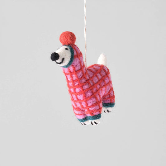 A handcrafted felt llama ornament hanging from a thin white string against a solid light gray background. The llama is made of pink and red patterned wool with white accents on its face, legs, and tail, and dark teal accents around its neck and hooves.