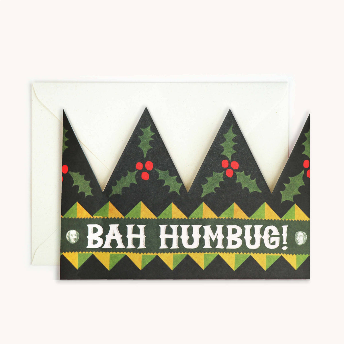 A Christmas-themed greeting card with a crown-shaped black border, green holly leaves, red berries, and the text 'BAH HUMBUG!' in white, shown with a white envelope behind it on a light background.
