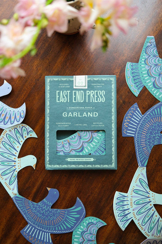 Pack of 'East End Press Garland' on a wooden surface with decorative cut-out shapes.