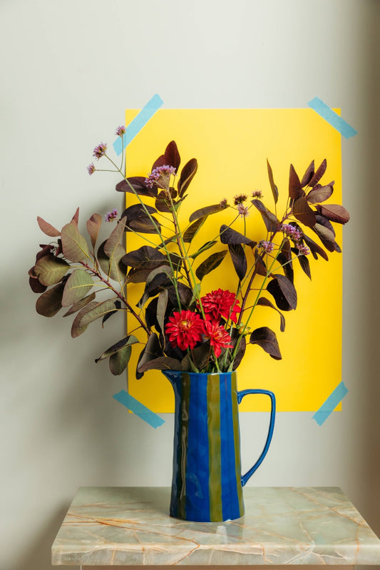 Blue vase with red flowers on a marble surface against a yellow background