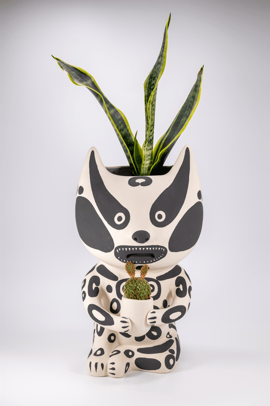 A ceramic planter by Grayson Perry in the shape of a stylized character with a black and white pattern, holding a green plant.