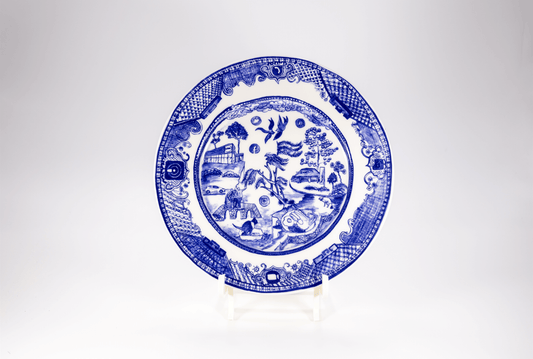 A glazed ceramic plate with a blue design featuring elements of 'normal life' such as a full English breakfast and video conferencing, displayed against a white background.